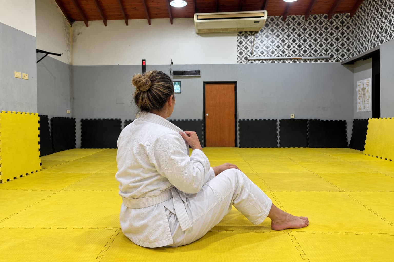 Una persona sentada en el tatami ajustando el gi, con la cara oculta.