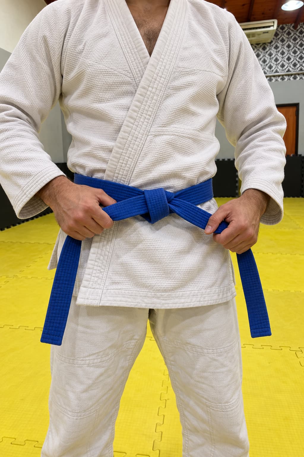 Manos atando un cinturón azul sobre un gi blanco.